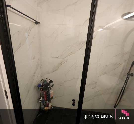 מקלחון עם דלת זכוכית ומדף מוצרי רחצה